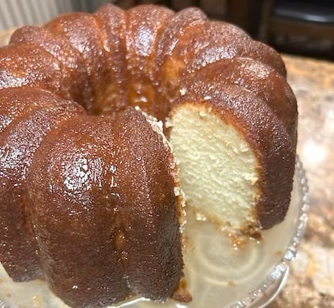 Kimi D's butter-glazed pound cake on a glass cake stand, one slice cut away to show the soft, moist crumb