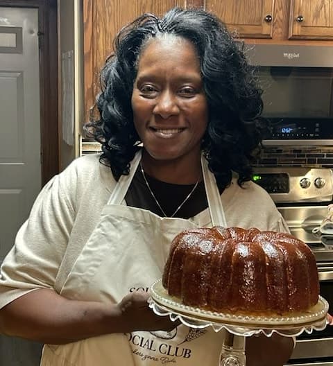 Kim Davenport smiling in her Canton, Ohio kitchen, holding a butter-glazed pound cake on a glass cake stand